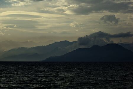 Seascape of the cloudy coastline with foggy mountains and sea in the sunset.の写真素材