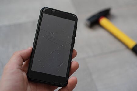 Man holding smartphone with broken touchscreen on the hammer background. Unsuccessful Ñrush test...