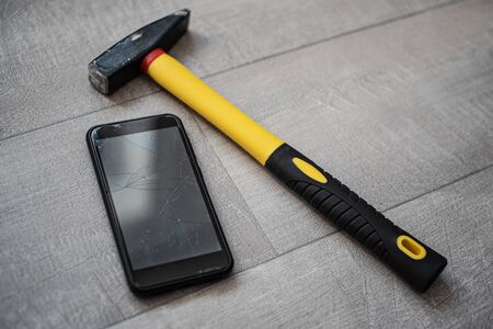Man holding smartphone with broken touchscreen on the hammer background. Unsuccessful Ñrush test if the protective glassの写真素材