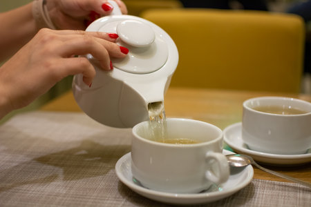 female hands pour tea into a cup during breakfast for two person in a restaurantの写真素材