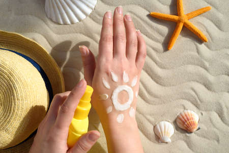 Hands with sunscreen. Seashells, starfish, sun hat, sunscreen and hand with cream. The concept of...