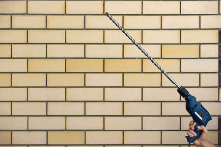 hand with a drill on the background of a brick wall. Renovation and constructionの写真素材