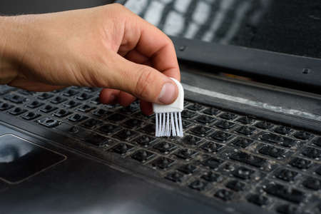 Male hand cleans dirty keyboard without keys with a brush