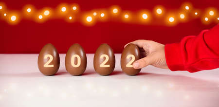 The inscription 2022 on the chocolate eggs. A child's hand reaches out for a sweet gift. Christmas...