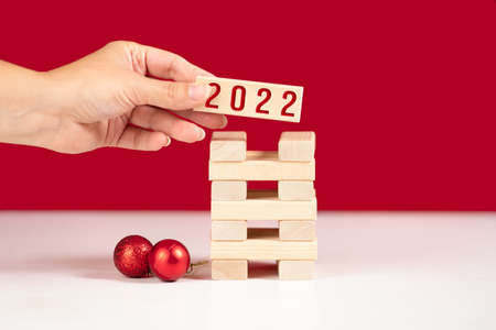 Female hand puts the stick wiwt inscription 2022 on the children's game. Red background with...