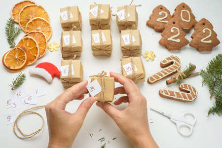 Female hands packages gifts for advent calendar. Preparing for Christmas with gingerbread cookies, dried oranges, sprigs of fir. Eco friendly new year holidaysの写真素材