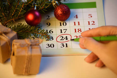 A woman's hand marks the date December 24 on the calendar. Preparing for christmas with spruce and new year decorations and giftsの写真素材