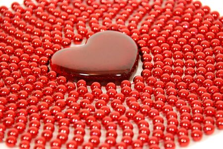 Beads stringed together to make an interesting texture around a red glass heart symbolizing love and romanceの写真素材