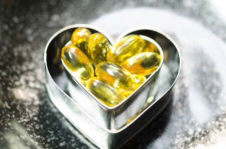 fish oil capsule on double heart shape box in smaller one  on black plateの写真素材