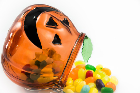 Jelly beans drop from pumpkin glass container isolated on white backgroundの写真素材
