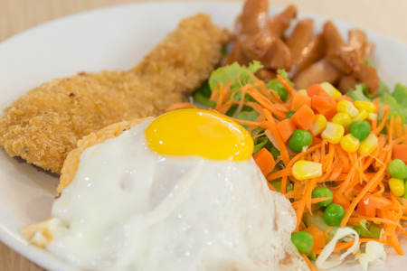 Thai American fusion style fried rice with fried egg and fried chicken served with salad closeup focused on yolkの写真素材