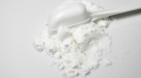 Scoop of White Collagen amino protein powder  poured with spoon isolated on white background