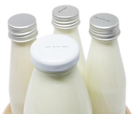 Soy milk bottles with big one in front and three thin ones back on wooden plate isolated on white...