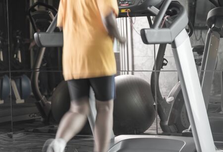 Unknown woman running with treadmil in gym back side with speed blur from running in yellow shirt
