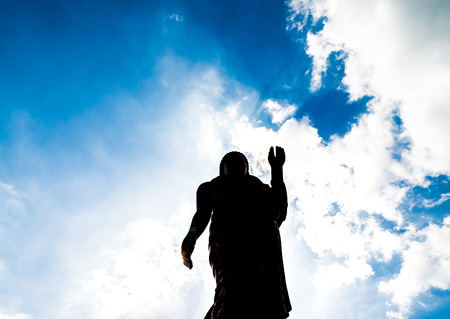 Buddha statue ok sign post bottom view with dark silhouette with deep clear blue sky with few clouds and white light glowingの写真素材