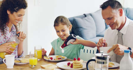 Start each morning with the people who matter the most. Shot of a cute little girl having breakfast with her parents in the morning at home.の写真素材