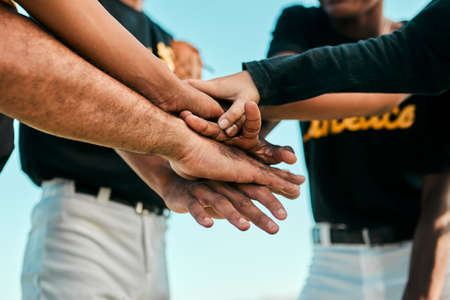 They all work together for a single purpose. Shot of a team of young baseball players joining their hands together in a huddle during a game.の写真素材