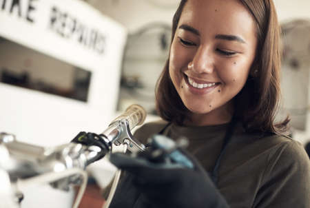 You look as good as new. Shot of an attractive young woman standing alone in her shop and repairing a bicycle.の写真素材