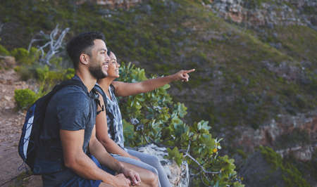 Look at how amazing that view is. Shot of a young couple enjoying the sunset view while out on a hike on a mountain range.の写真素材