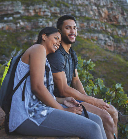 Sunsets are better with you by my side. Shot of a young couple enjoying the sunset view while out on a hike on a mountain range.の写真素材