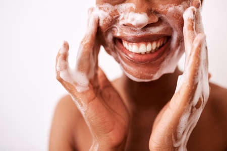 I wash my face twice a day. Studio shot of an unrecognizable woman washing her face against a white background.の写真素材