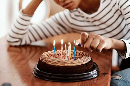 Birthdays in quarantine...not cool. Cropped shot of a woman lighting candles on a birthday cake at home and looking sad.の写真素材