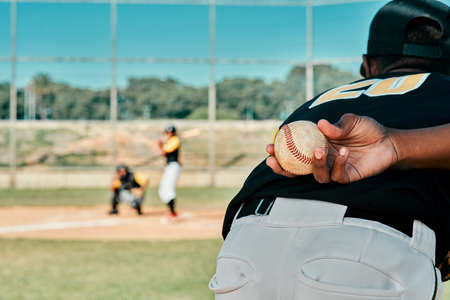 My team game to win. Rearview shot of a baseball player holding the ball behind his back.の写真素材