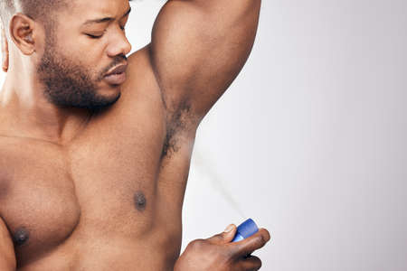 Grooming is vital for any gentleman. Studio shot of a handsome young man spraying deodorant on his armpit against a white background.の写真素材