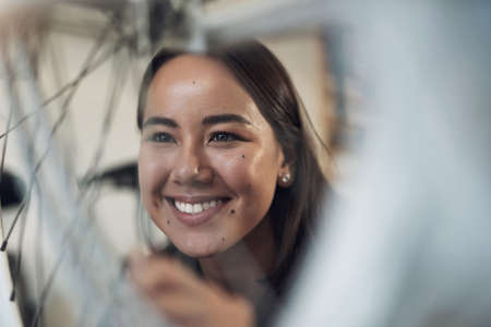 This looks as good as new. Shot of an attractive young woman crouching alone in her shop and repairing a bicycle wheel.の写真素材