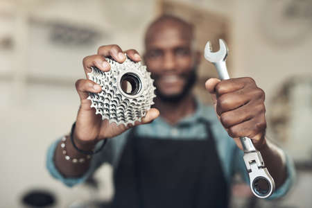 This is literally all you needed for your bike. Shot of an unrecognizable man standing alone in his bicycle shop while holding a spanner and bicycle cassette.の写真素材