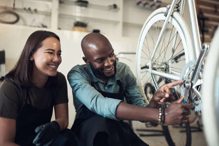 I fixed that. Shot of two young business owners crouching in their shop and fixing a bicycle wheel.の写真素材