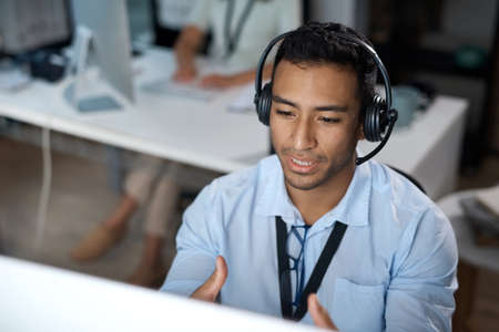 When youre not sure, hell show you the way. Shot of a young man using a headset and computer in a modern office.の写真素材