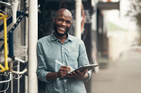 Are you ready to see your bike. Shot of a handsome young man standing alone outside his bicycle shop and writing on a clipboard.の写真素材