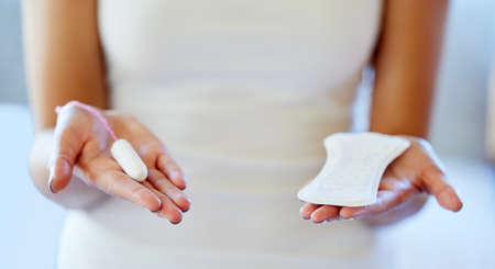 Which one do you prefer. Cropped shot of an unrecognizable woman holding a tampon and a pad in her...