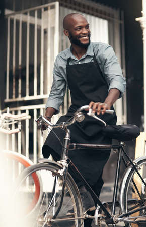 Im the citys best bike salesman. Shot of a handsome young man moving a bicycle from his shop during the day.の写真素材