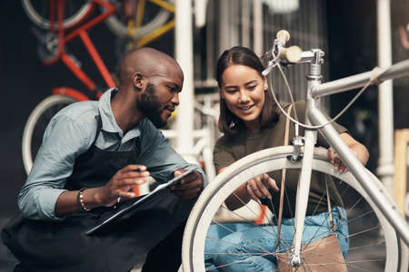What is this over here. Shot of a handsome young man crouching outside his bicycle shop and assisting a customer.の写真素材