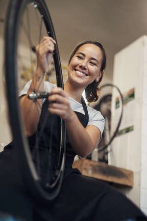 Theres nothing a brand new tyre cant fix. Shot of an attractive young woman standing alone in her shop and repairing a bicycle wheel.の写真素材