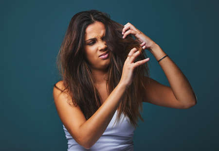 Messy hair, I CARE. Studio shot of a beautiful young woman pulling on her hair posing against a blue background.の写真素材