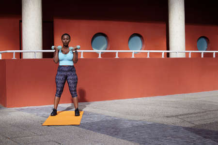 Your core/ your breath/your anchor. Shot of a young woman using dummbells on a gym mat against an...