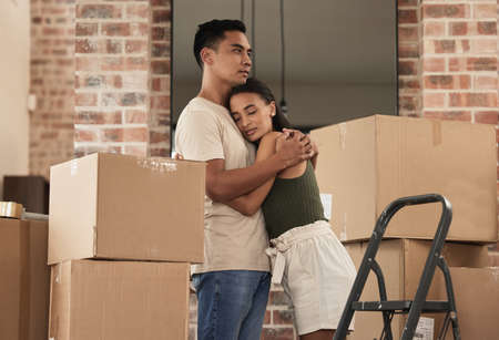 Lets, stay together. Shot of a young couple hugging in to their new home.