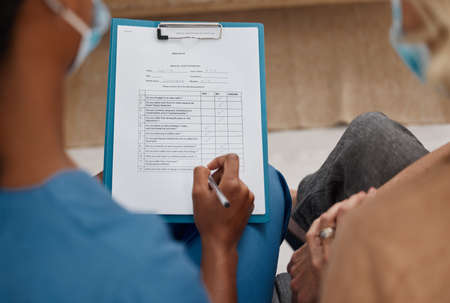 A thorough consultation starts with a concise medical history. Shot of a doctor filling out a questionnaire during a consultation with a senior woman at home.の写真素材