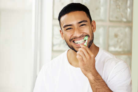 This is the best toothpaste, the proof is in my smile. Shot of a handsome young man brushing his teeth at home.の写真素材