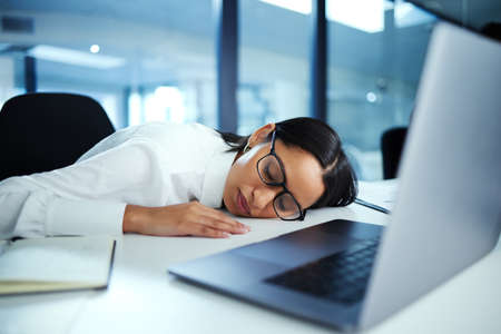 Ive been so tired lately. Shot of a young businesswoman taking a nap at her desk.の写真素材