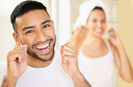 Flossing is just as important as brushing your teeth. Shot of a happy young couple flossing their teeth in the bathroom at home.の写真素材