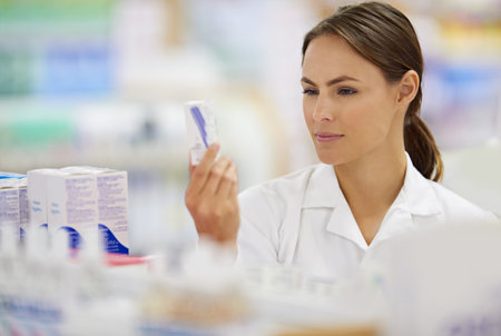 Finding the perfect treatment. Shot of an attractive young pharmacist collecting a prescription in an aisle.の写真素材
