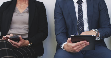 Technology helps to pass the time. 4k video footage of a group of businesspeople using digital devices while sitting in a line against a white background.の写真素材