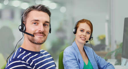 How can we make a difference. Portrait of two business colleagues wearing headsets in the office.の写真素材