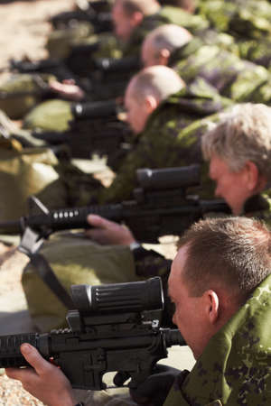 Aiming low. A line of soldiers lying and aiming with their guns.