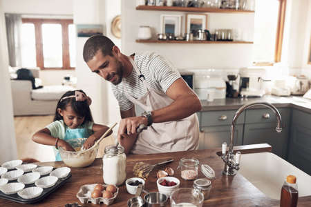 Bake someone happy. Shot of a father teaching his daughter how to bake in the kitchen at home.の写真素材