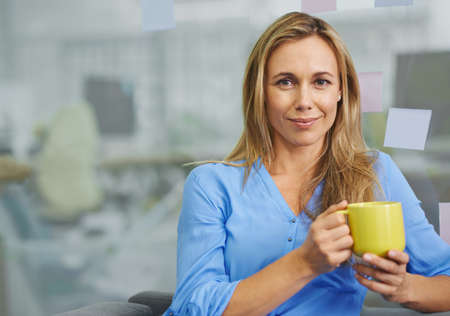 I cant work without my coffee. Attractive blonde female employee having her coffee break.の写真素材